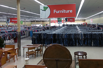 Wooden table and chairs in the furniture department and racks of clothes in the distance.